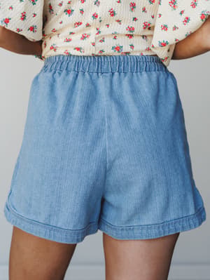 A back-view close-up of relaxed chambray shorts with an elastic waistband, styled with a floral print cropped top — easy, warm-weather dressing that feels effortless without trying.