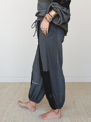 A side-angle shot of relaxed harem-style jogger pants in charcoal, styled with a matching oversized sweatshirt and stacked boho jewelry — the kind of outfit that somehow looks intentional even at 8am.