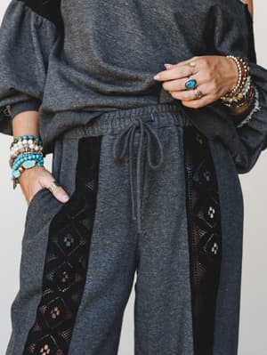 A close-up mid-shot of a charcoal matching set — relaxed sweatshirt and lace-panel joggers — styled with an armful of stacked turquoise and mixed-bead bracelets and a turquoise cocktail ring, giving the whole look a boho edge that makes 'comfy day' f