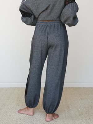 Shot from behind, a model wears a matching charcoal fleece jogger and cropped sweatshirt set with black crochet lace side panel detailing — cozy and relaxed with just enough of an unexpected edge.