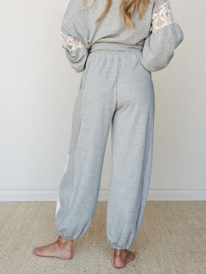 A back-view shot of a relaxed heather grey jogger set with crochet lace panel detailing on the sleeves and pant leg — the kind of outfit that makes staying home feel intentional.