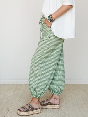 A side-profile shot of green gingham balloon-style joggers paired with a white tee and leopard print platform sandals — playful and relaxed with a stacked bracelet moment that pulls it all together.