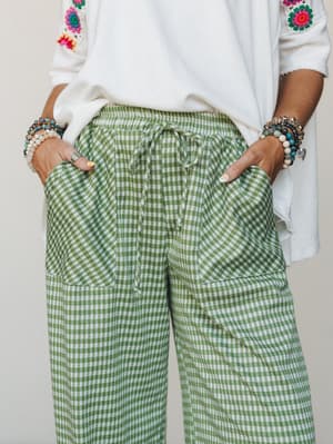 A mid-shot of green gingham jogger pants styled with a white crochet-trimmed top and stacked bracelets — the kind of easy, expressive outfit that feels just as good as it looks.