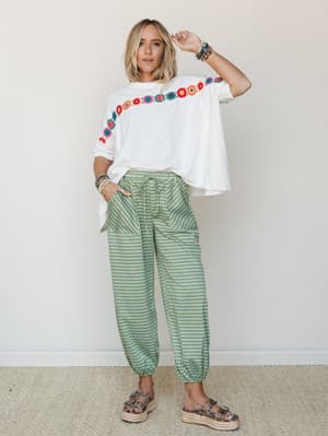 A relaxed, colorful outfit pairing oversized white tee with diagonal floral embroidery against green gingham joggers — the kind of look that makes a Tuesday feel a little more fun.