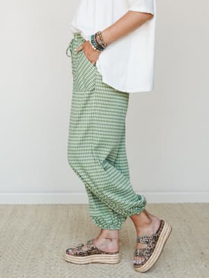 A side-profile shot of green gingham jogger pants styled with a relaxed white tee, stacked bracelets, and leopard print platform sandals — effortlessly casual with just enough personality.