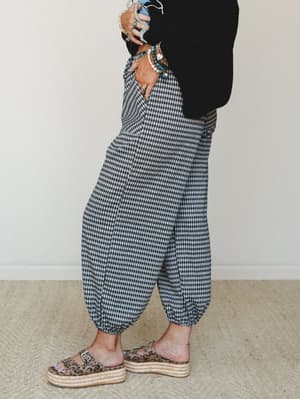 A side-profile shot of gingham jogger pants styled with a black sweater, leopard print platform sandals, and a stack of boho bracelets — relaxed and personality-forward.