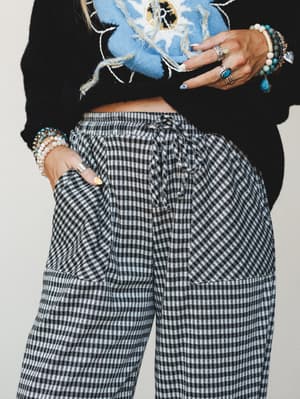 A close-up mid-shot of black and white gingham jogger pants styled with a cropped black sweater and layered boho jewelry — stacked bracelets, statement rings, and turquoise — giving the outfit an effortlessly collected, personality-first feel.