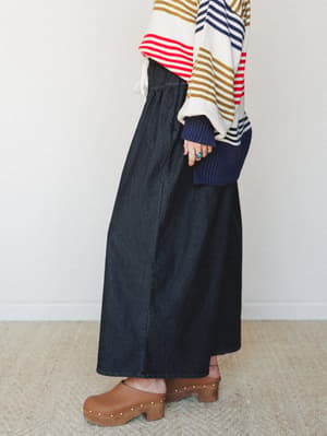 A side-profile shot of a dark denim wide-leg pant styled with a multicolor striped oversized sweater and warm brown studded clogs — the kind of effortless, personality-forward outfit that looks like it came together in five minutes but somehow hits e