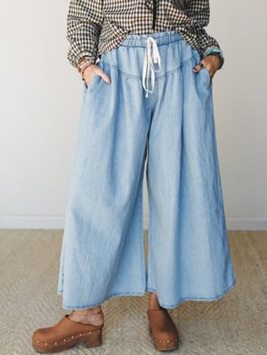 Wide-leg chambray pants with a relaxed drawstring waist styled with a gingham top, stacked beaded bracelets, and wooden clogs — easy, expressive dressing that looks effortless without trying.