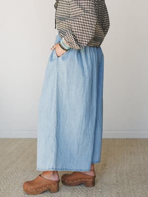 A side-profile shot of a wide-leg light denim pant styled with a black and cream gingham top and wood-heel clogs — relaxed, lived-in, and the kind of outfit you reach for on a day when you want to feel pulled together without trying too hard.