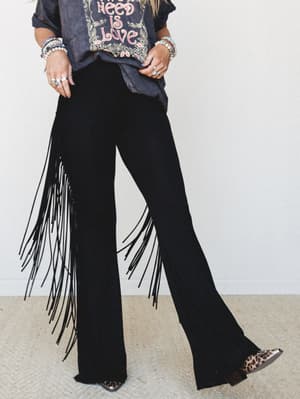 Black flare pants with dramatic side fringe steal the scene, styled with a washed graphic tee, stacked bead bracelets, and leopard cowboy boots for a look that's equal parts rock and rodeo.