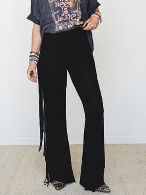 Black flare pants with dramatic side fringe styled with a washed graphic tee, stacked bead bracelets, and leopard print booties — the kind of outfit that shows up to the concert and doesn't need to explain itself.