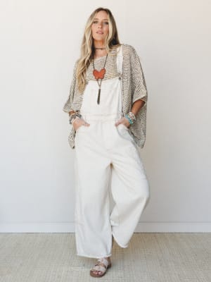 Wide-leg ivory overalls layered under an open-knit oversized poncho, styled with stacked turquoise bracelets, a statement stone pendant, and neutral sandals — the kind of effortless outfit that looks like it came together in five minutes but absolute