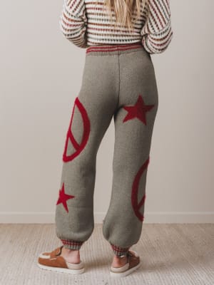 Person wearing gray knit pants with red star and peace symbol patterns, standing against a plain background.