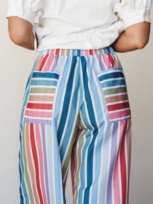 A close-up back view of wide-leg multicolor striped pants with patch pockets, paired with a white short-sleeve top — playful and relaxed with a serious commitment to color.