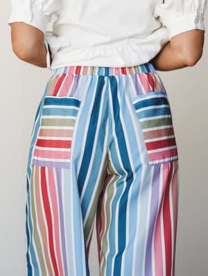 A close-up back view of wide-leg multicolor striped pants with patch pockets, paired with a white short-sleeve top — playful and relaxed with a serious commitment to color.