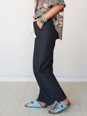 A side-profile shot of wide-leg black denim styled with a floral print top, sky blue buckle sandals, and a stack of beaded bracelets — casual and collected with just enough personality.