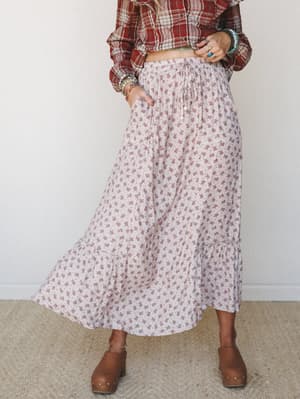A tiered floral maxi skirt in soft blush-taupe paired with a cropped red plaid top and brown clogs — the kind of outfit that looks like it came together effortlessly but was absolutely thought through.