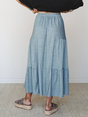 A flowy heather teal tiered maxi skirt styled from the back with a black crop top and leopard espadrilles — the kind of effortless outfit that looks like you tried just enough.