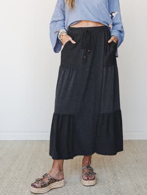A tiered maxi skirt in two-tone charcoal styled with a breezy blue long-sleeve top and leopard print flatform sandals — the kind of effortless outfit that works just as hard on a coffee run as it does at a weekend farmers market.