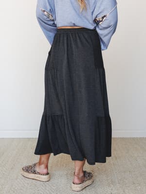 A back-view shot of a tiered charcoal maxi skirt styled with a flowy blue long-sleeve top and leopard print platform espadrilles — casual and collected with just enough personality.
