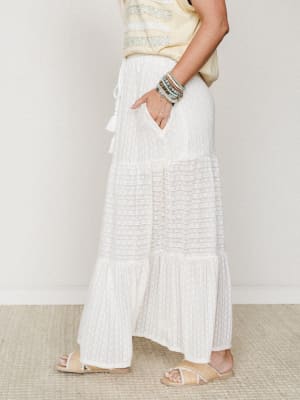 A side-profile shot of a cream tiered maxi skirt with textured stripe detailing, styled with a soft yellow embroidered top, woven sandals, and a stack of turquoise and earth-tone bracelets — effortless and easy, like a slow morning that turned into a