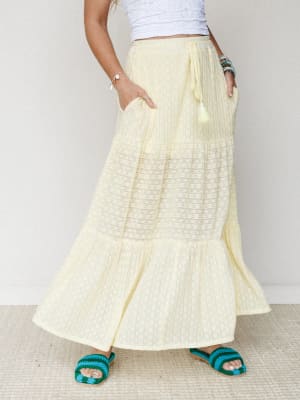 A breezy butter-yellow maxi skirt with tiered lace inset panels and a tassel drawstring waist, styled with a white eyelet crop top and crochet sandals — the kind of outfit that makes a Tuesday feel like a vacation.