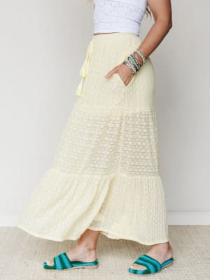 A sun-washed tiered maxi skirt in soft butter yellow pairs with a white lace crop top and teal crochet sandals — the kind of outfit that makes a Tuesday feel like a trip somewhere warm.