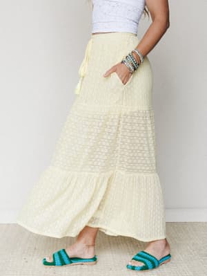 A sun-washed tiered maxi skirt in soft butter yellow pairs with a white lace crop top and teal crochet sandals — the kind of outfit that makes a Tuesday feel like a trip somewhere warm.