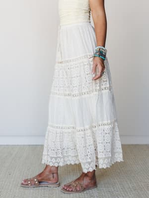 A dreamy ivory maxi skirt with tiered lace panels and scalloped hem, styled with studded sandals and a stack of turquoise beaded bracelets — the kind of outfit that feels equally at home at a garden wedding or a breezy afternoon in the sun.