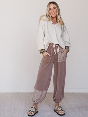 Woman wearing a light gray sweatshirt and brown pants with a white background