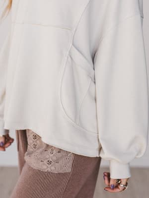 Close-up of a person wearing a light-colored sweater and brown pants with lace details.