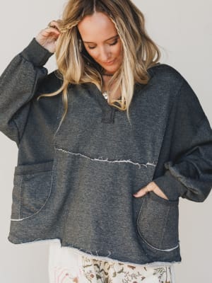 Woman wearing a dark gray oversized hoodie with white trim on a plain background