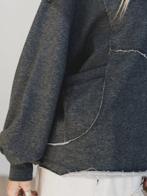 Close-up of a dark gray denim jacket with frayed hem on a plain background