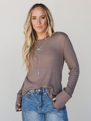 Woman wearing a brown waffle knit top and blue jeans against a plain background