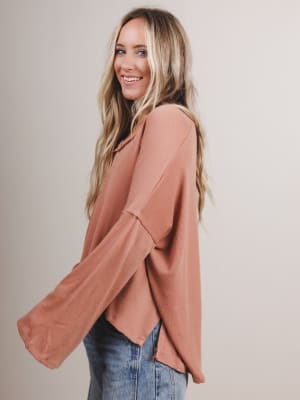 Woman wearing a peach boho top with long sleeves against a plain background