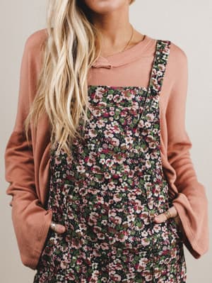 Woman wearing floral overalls over a peach top against a neutral background