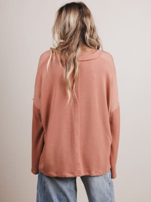 Back view of woman wearing a peach long-sleeve top with a neutral background