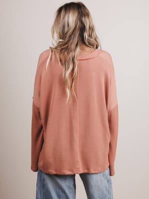 Back view of woman wearing a peach long-sleeve top with a neutral background