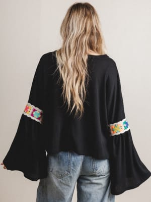 Back view of woman wearing a black blouse with colorful sleeve embroidery.