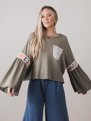 Woman wearing a green blouse with colorful sleeves and blue pants on a plain background