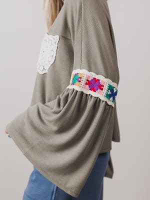 Green sweater with colorful crochet cuffs on a plain background