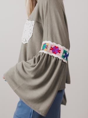Green sweater with colorful crochet cuffs on a plain background
