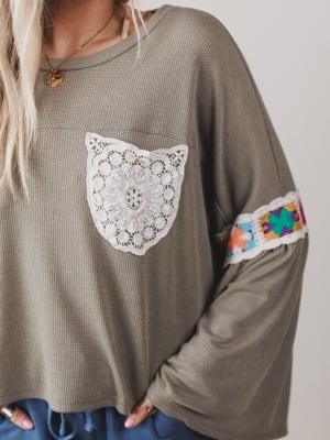 Green long-sleeve top with lace detail and colorful sleeves on a neutral background
