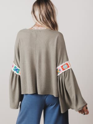 Person wearing a gray sweater with colorful sleeve embroidery on a plain background