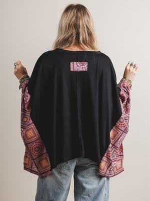 Back view of woman wearing a black top with colorful sleeves and a patterned patch on a plain background