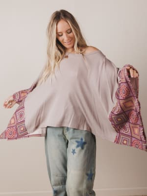 Woman wearing a loose-fitting beige top and jeans, holding a colorful patterned fabric.