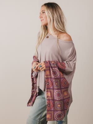 Woman wearing a long, patterned cardigan over a plain top with a neutral background