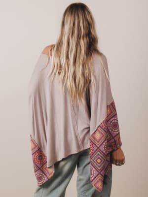 Person wearing a beige top with patterned sleeves against a plain background