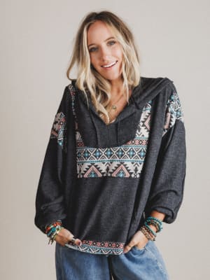 Woman wearing a dark gray hoodie with colorful tribal patterns on a plain background